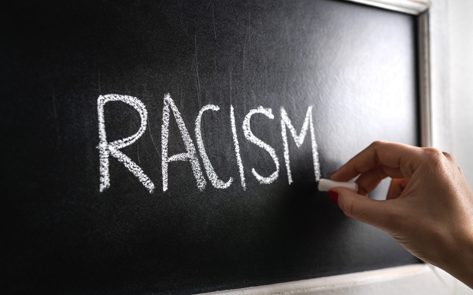 Hand writing the word racism on blackboard. Stop hate. Against prejudice and violence. Lecture about discrimination in school.