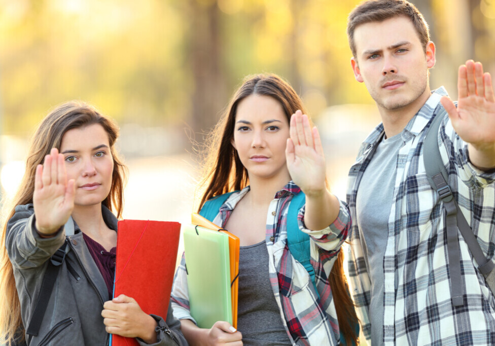 Three students gesturing stop in a park