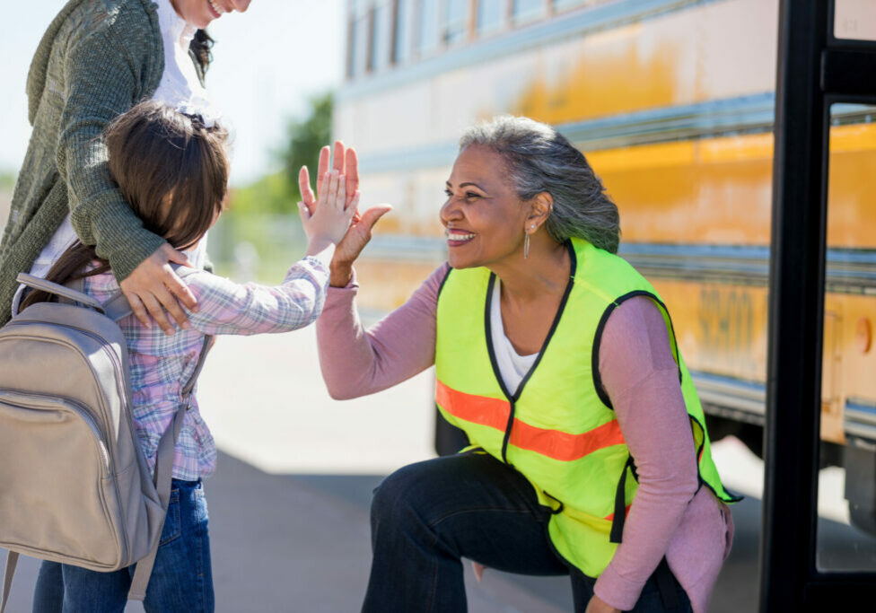 Senior female bus driver high-fives a new student