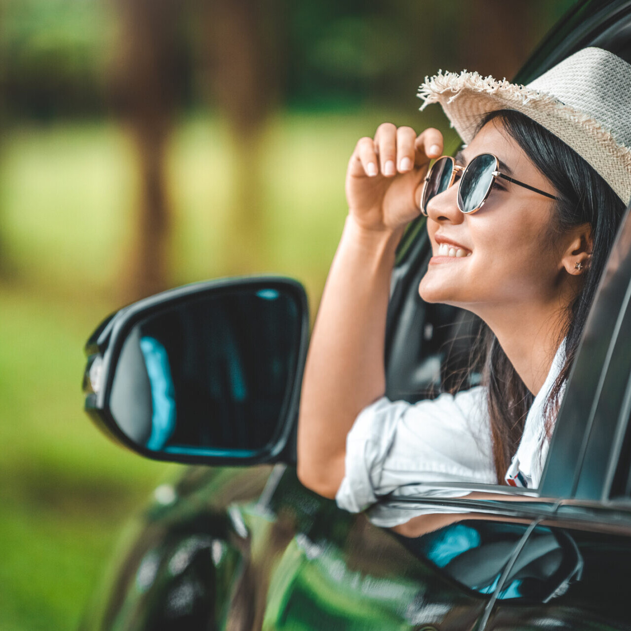 woman with sunglasses and a straw hat looking out of a car window