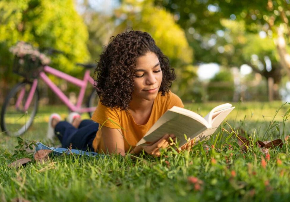Teen girl reading a book lying on the grass