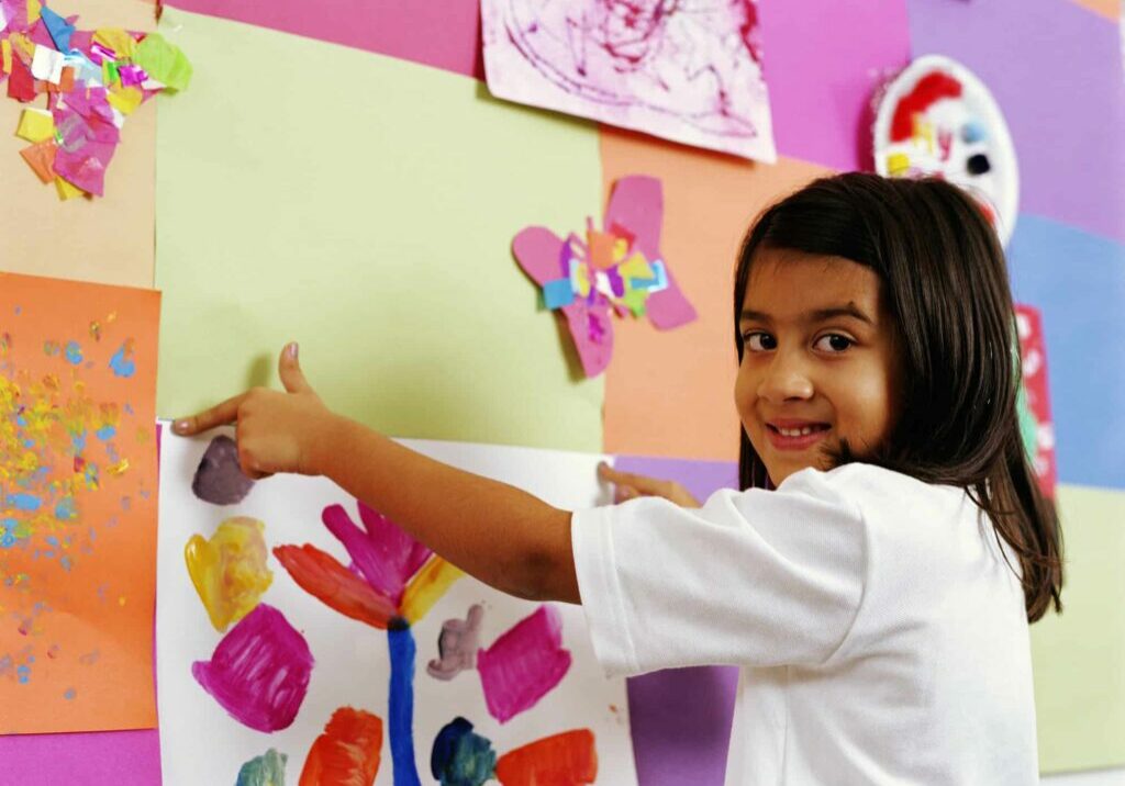 Schoolgirl (5-7) fixing painting to wall display