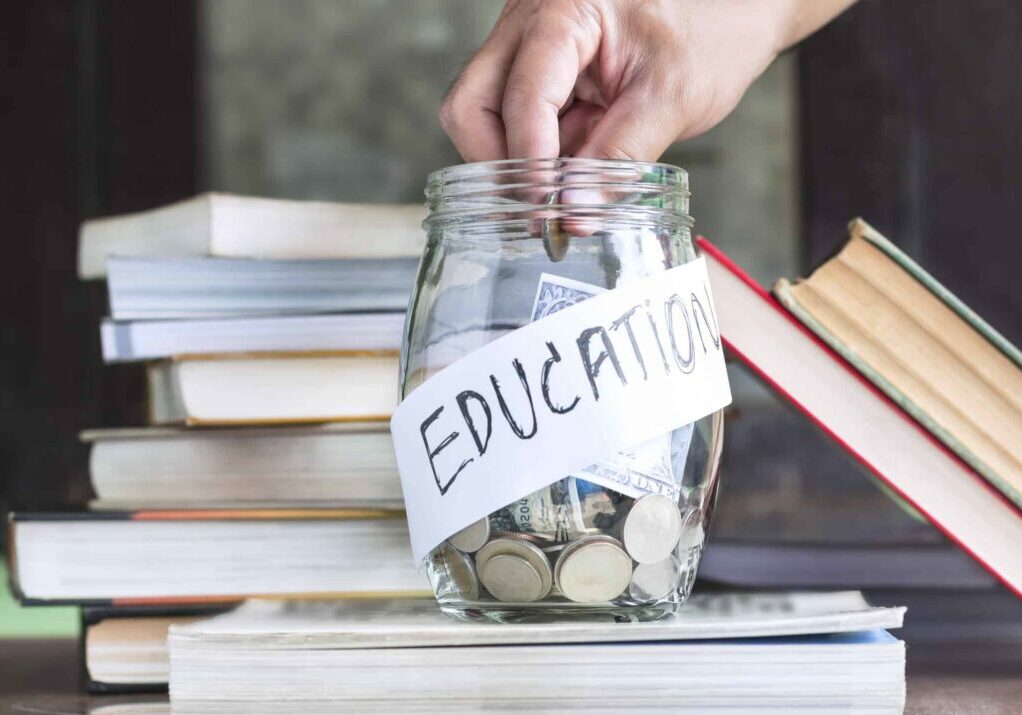 Coins and banknote in a glass jar placed on the textbook.