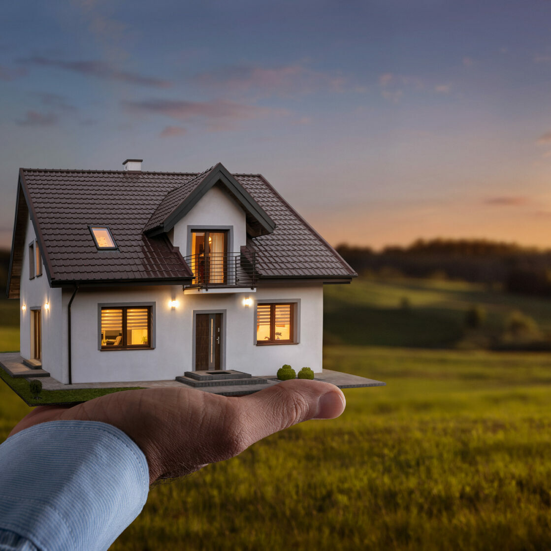 Concept of buying or building a new home. Male hand showing, offering a new dream house at the empty field with copy space