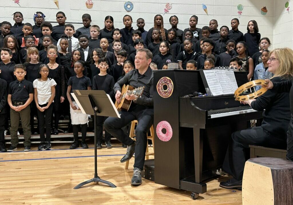 NJEA Vice President Steve Beatty accompanies Parkview Elementary School students on guitar for a winter concert. Professional musician Beverly MacDonald is on piano and tambourine. 