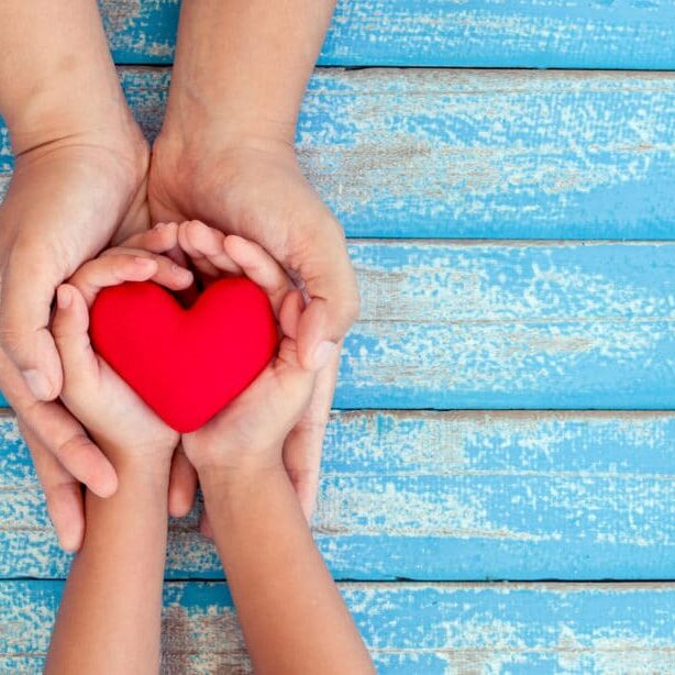 Red heart in child kid and mother hands on old blue wooden table